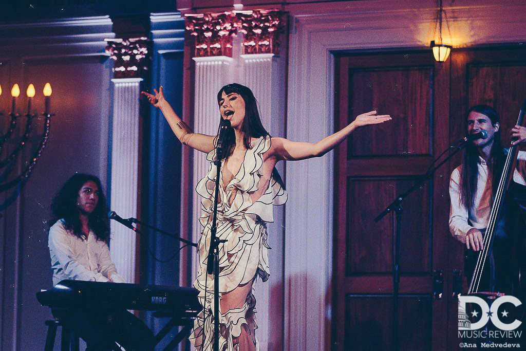 Kimbra throwing her hands up on stage and cocking her head to the side